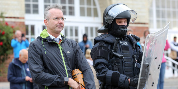 Nikolas Häckel steht während der freiwilligen Räumung des Punk-Protestcamps in Westerland auf Sylt neben einem Polizisten in Schutzausrüstung.
